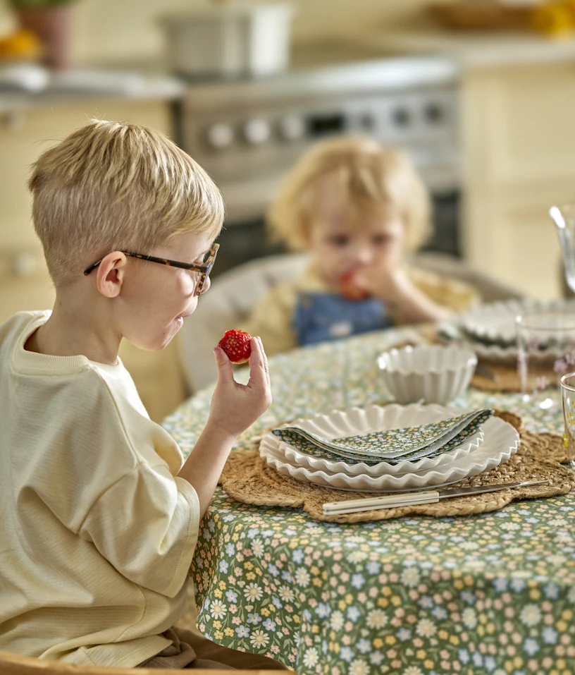 två barn sitter vid ett bord och äter jordgubbar