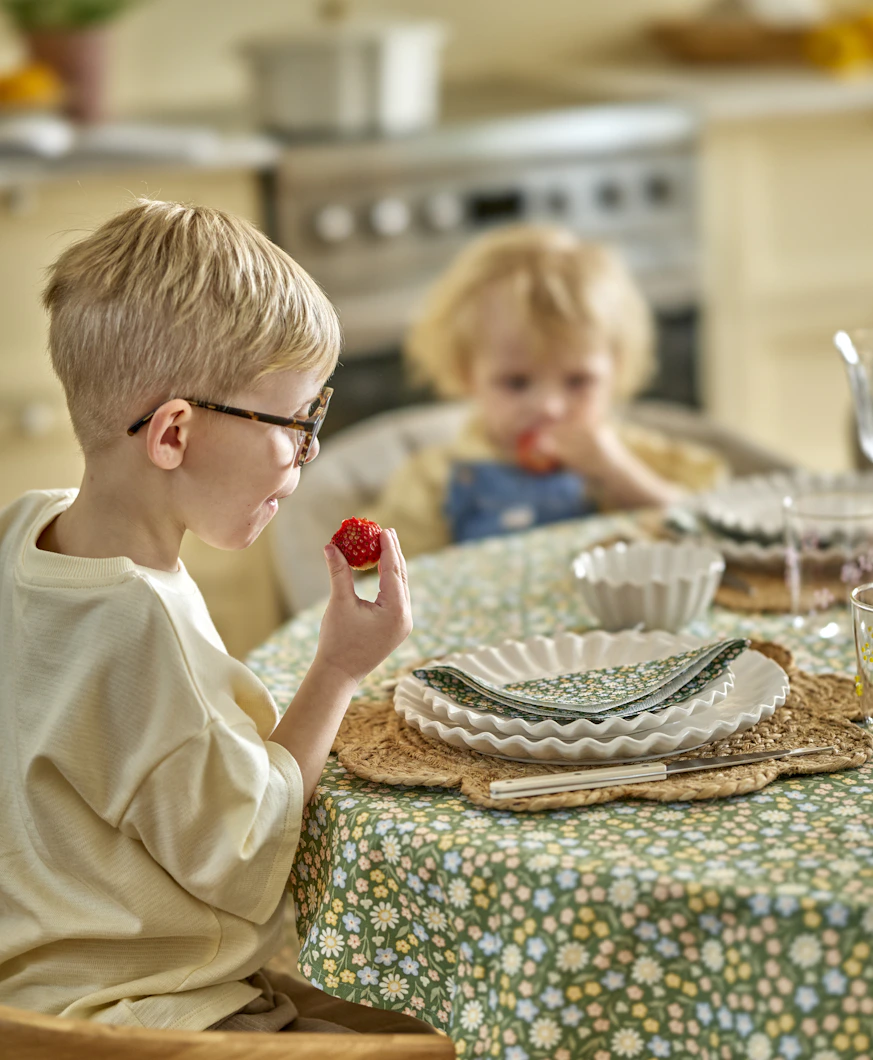 två barn sitter vid ett bord och äter jordgubbar