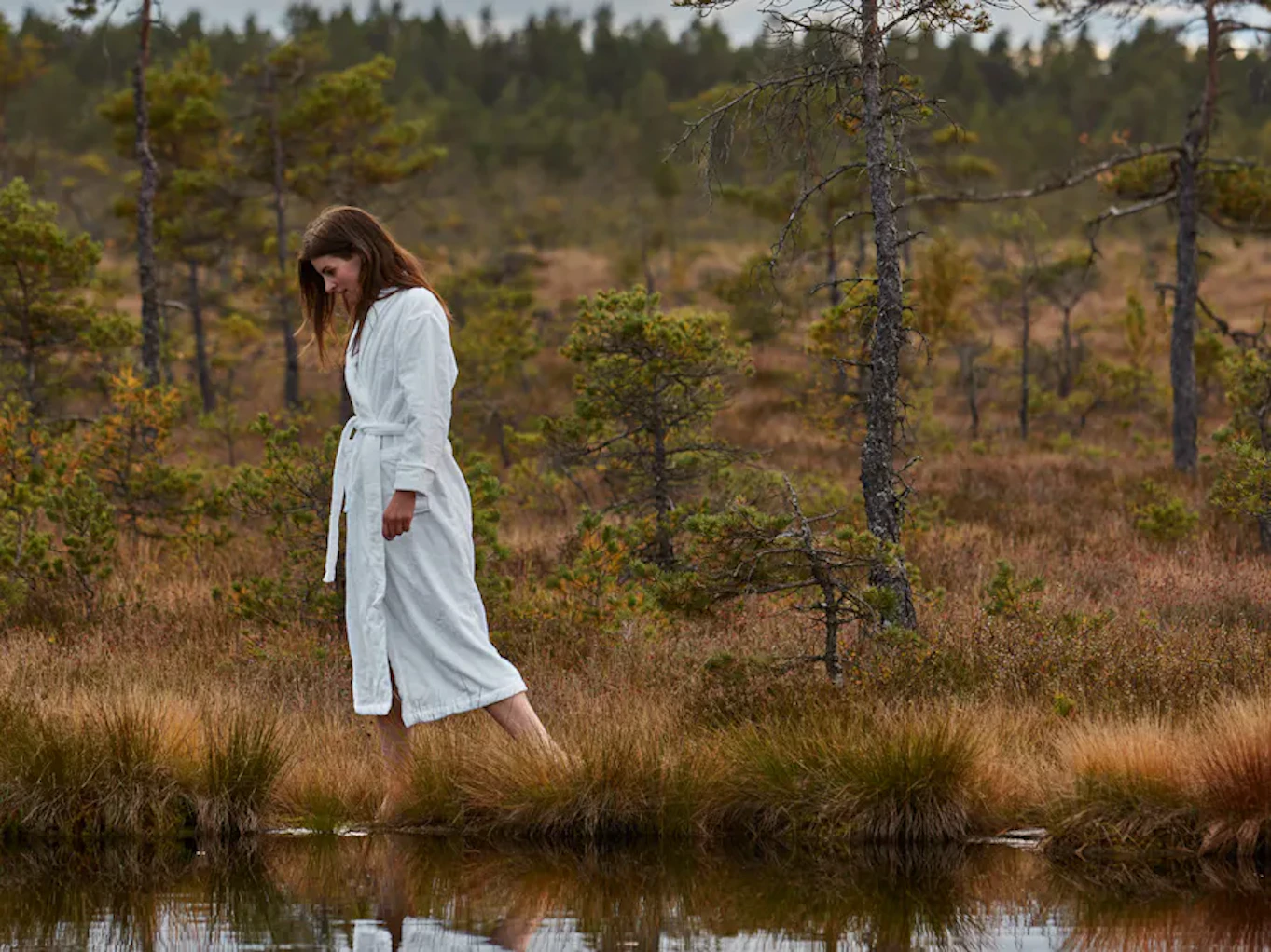 en tjej i morgonrock går bredvid vatten ute i naturen