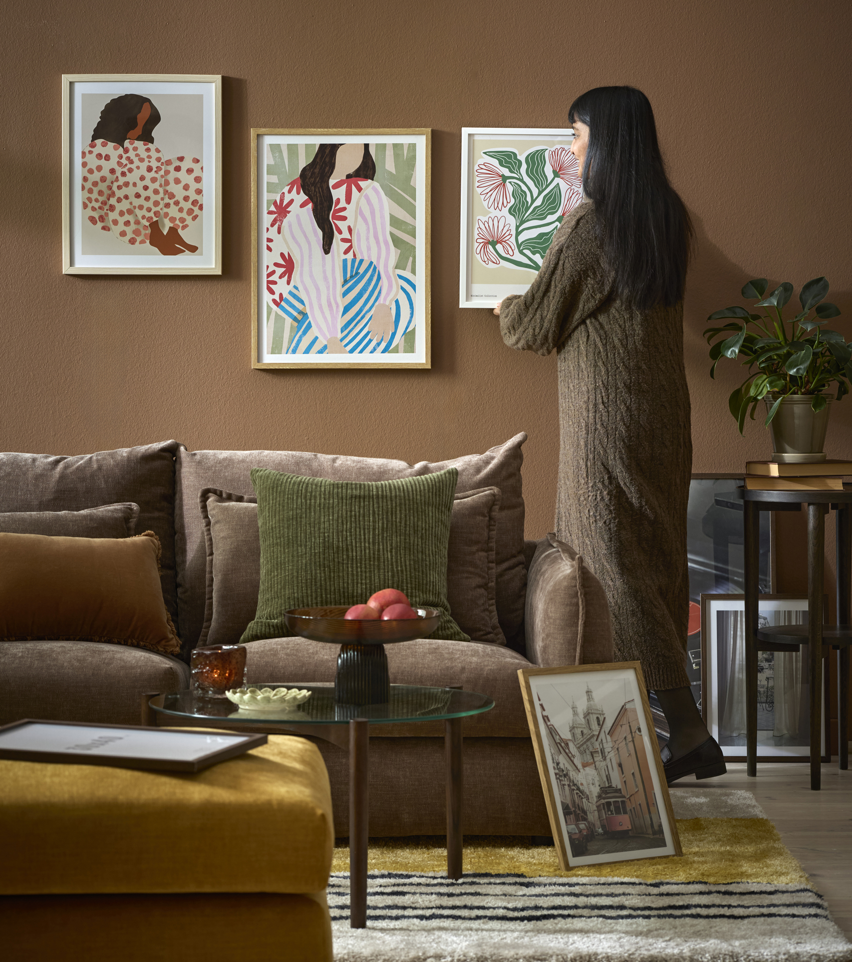 En kvinna hänger upp en färgglad tavla i ett vardagsrum med murriga toner