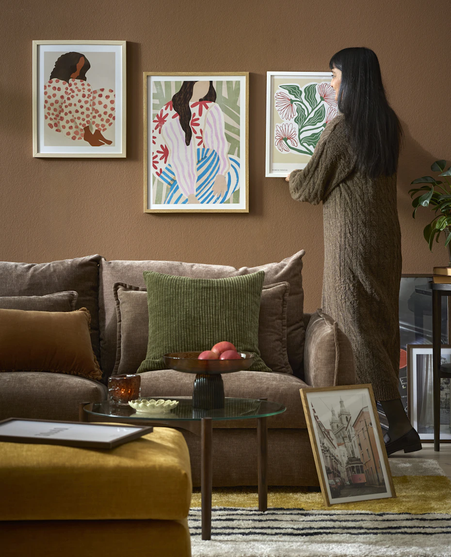 En kvinna hänger upp en färgglad tavla i ett vardagsrum med murriga toner