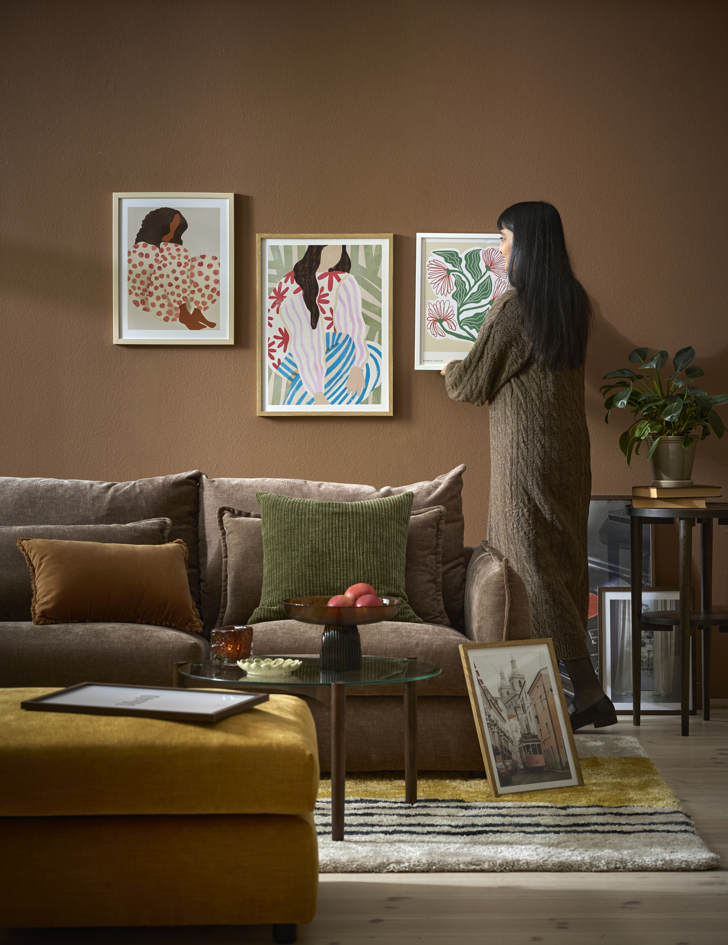 En kvinna hänger upp en färgglad tavla i ett vardagsrum med murriga toner