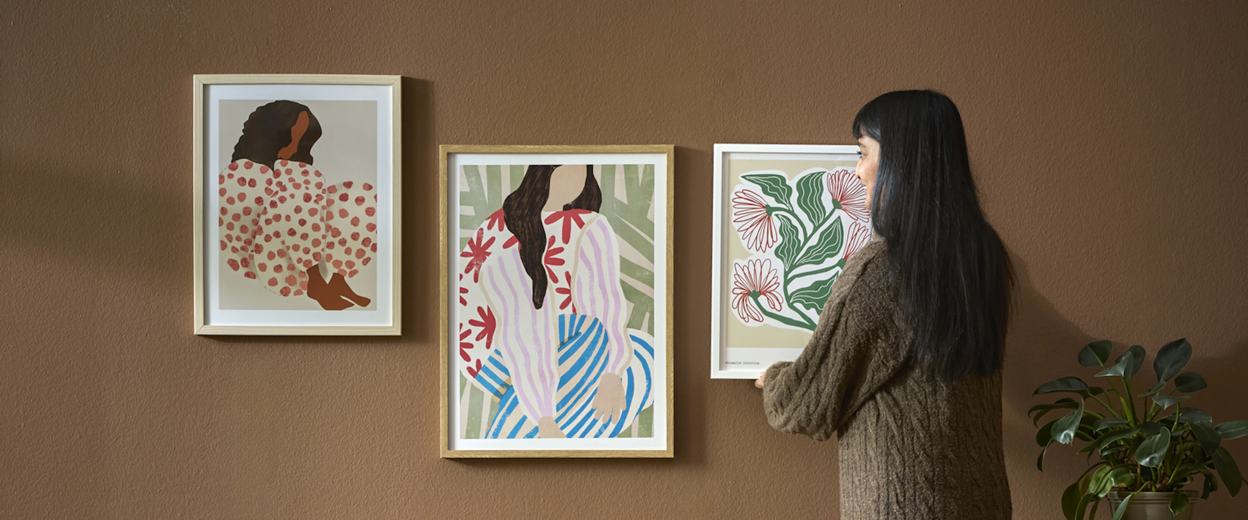 En kvinna hänger upp en färgglad tavla i ett vardagsrum med murriga toner