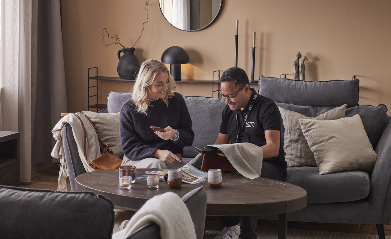 Butiksmiljö där butikspersonal från Mio sitter i en soffa tillsammans med kund och diskuterar tygprover för en soffa. 