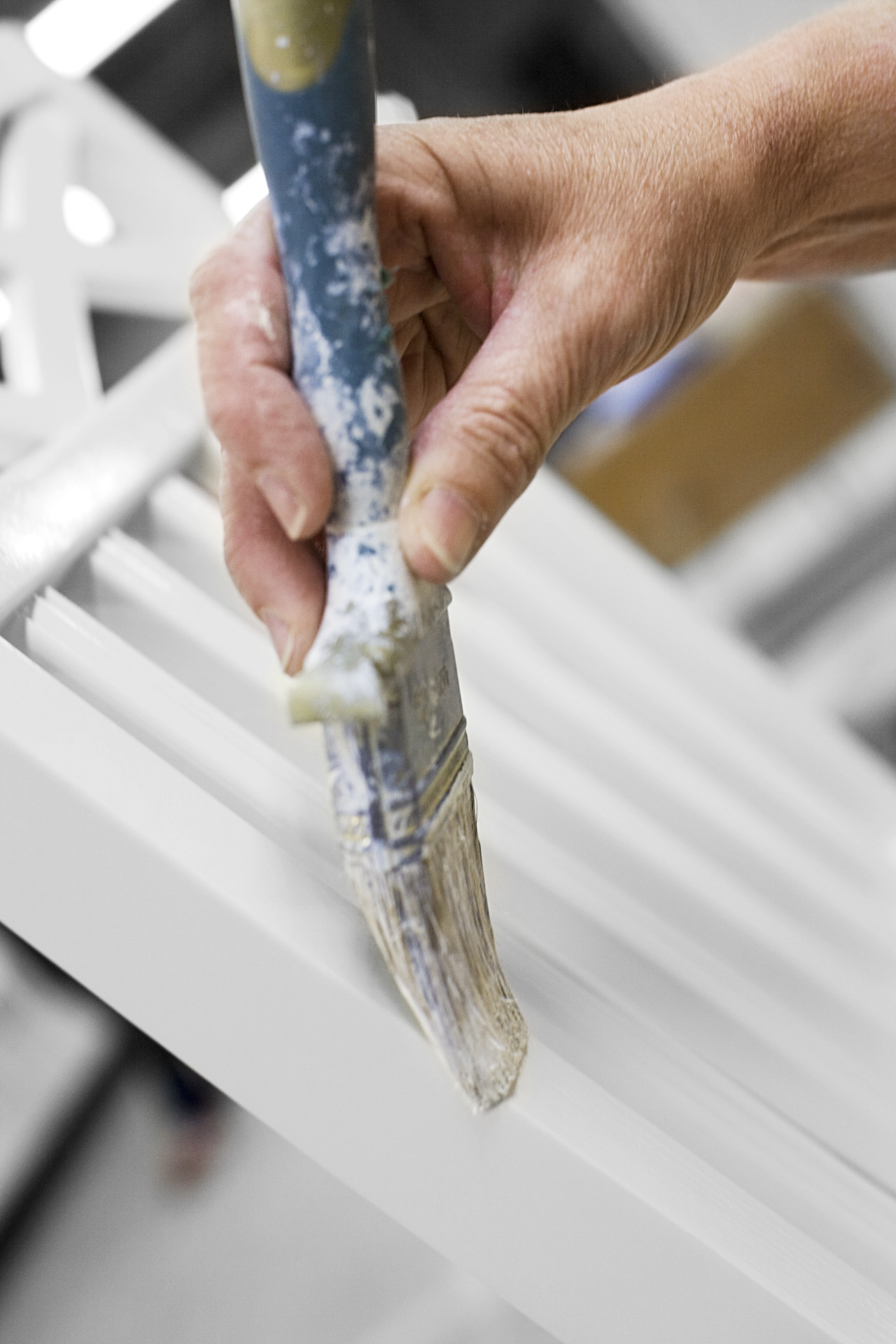 Närbild på hand som stryker pensel med vit färg över ribborna på en stolsrygg