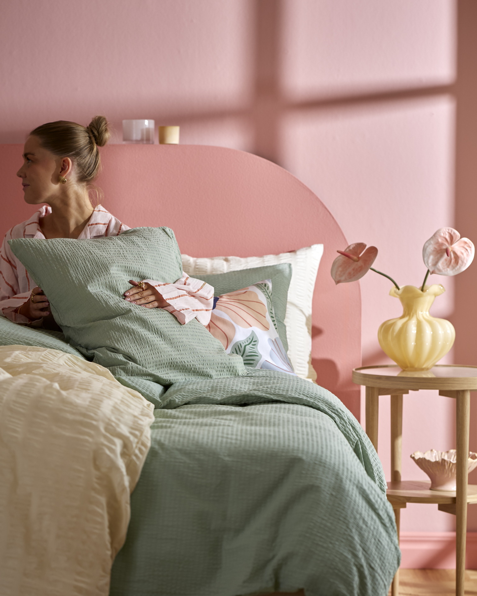 en tjej sitter i en säng i ett rosa sovrum och håller i en kudde med grönt örngott