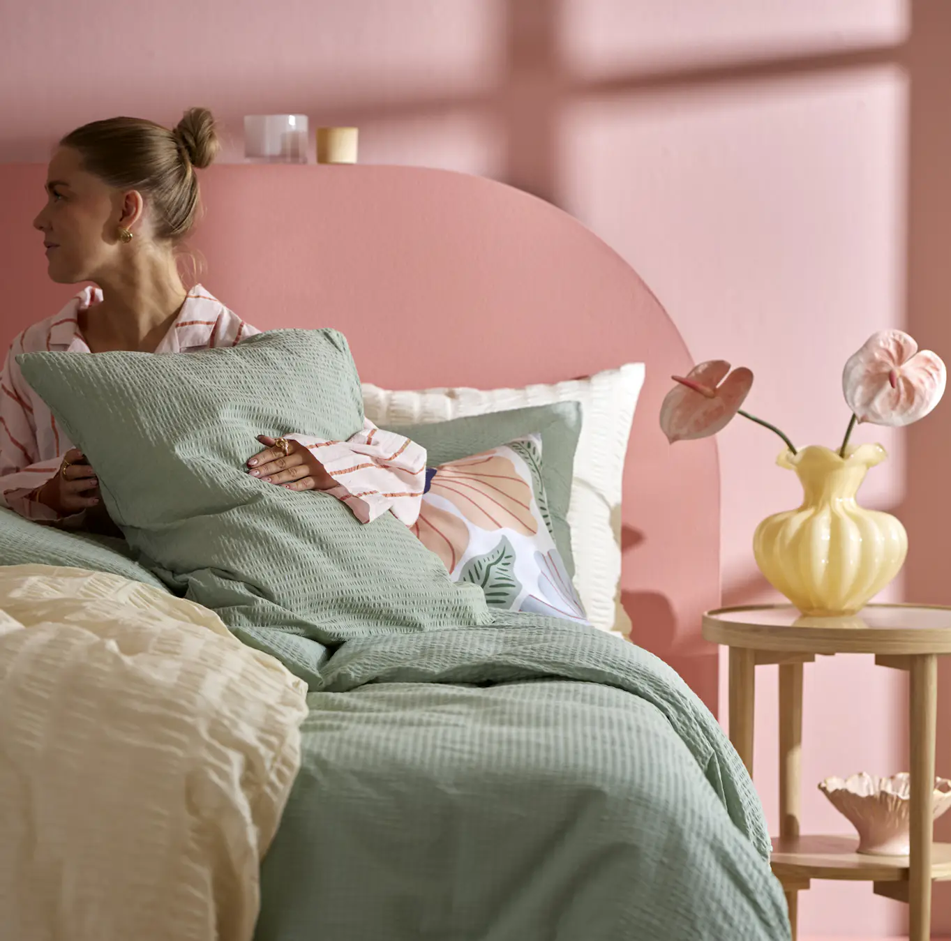 en tjej sitter i en säng i ett rosa sovrum och håller i en kudde med grönt örngott