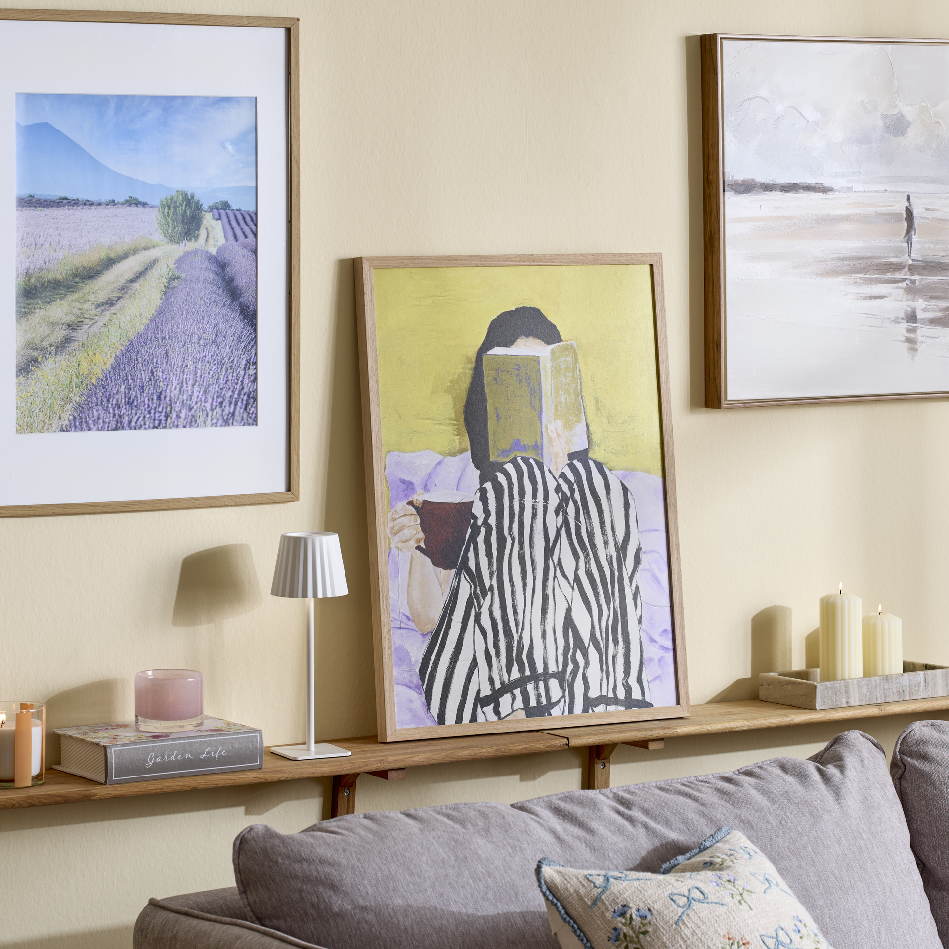 På hylla bakom en soffa står en lampa och en färgglad tavla, på väggen bakom sitter ytterligare tavlor