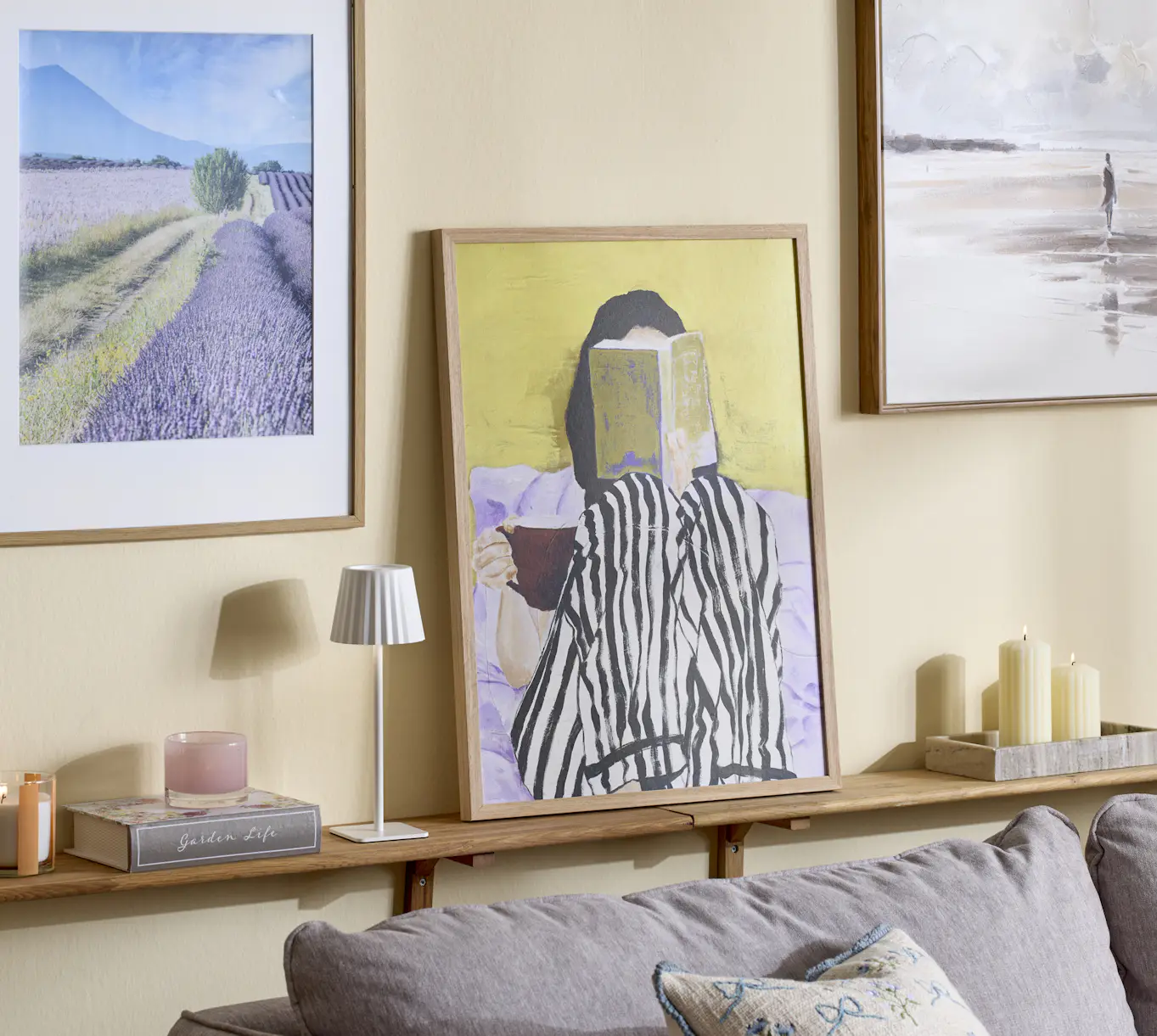 På hylla bakom en soffa står en lampa och en färgglad tavla, på väggen bakom sitter ytterligare tavlor