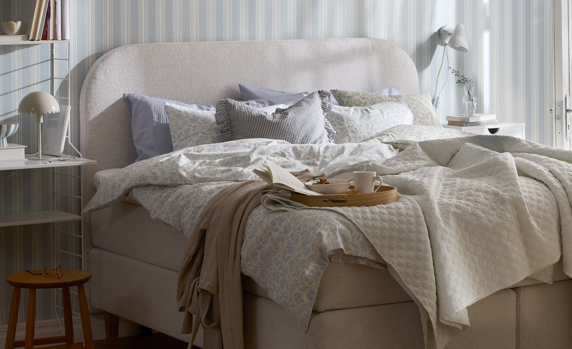 en grå kontinentalsäng med rundad gavel står i ett sovrum och är bäddad med påslakan i blåa toner