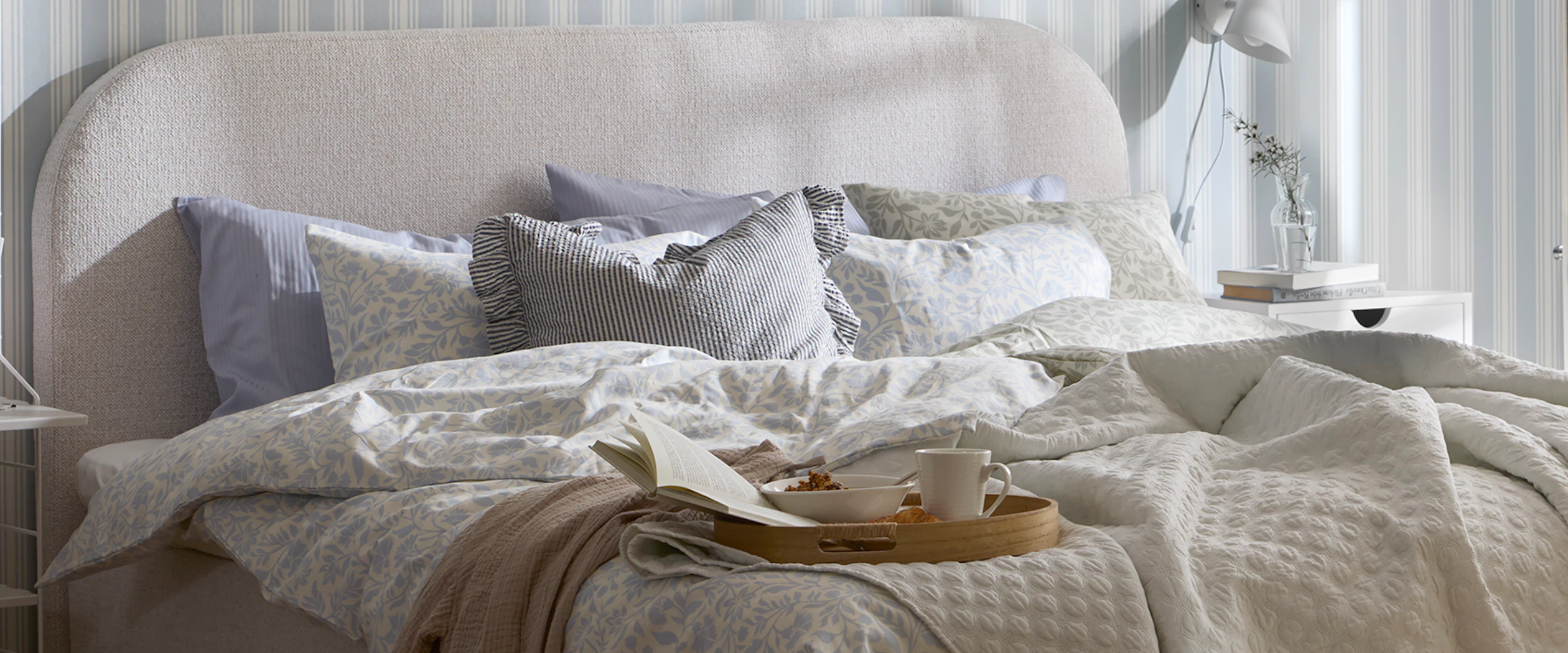 en grå kontinentalsäng med rundad gavel står i ett sovrum och är bäddad med påslakan i blåa toner