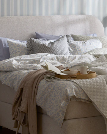 en grå kontinentalsäng med rundad gavel står i ett sovrum och är bäddad med påslakan i blåa toner