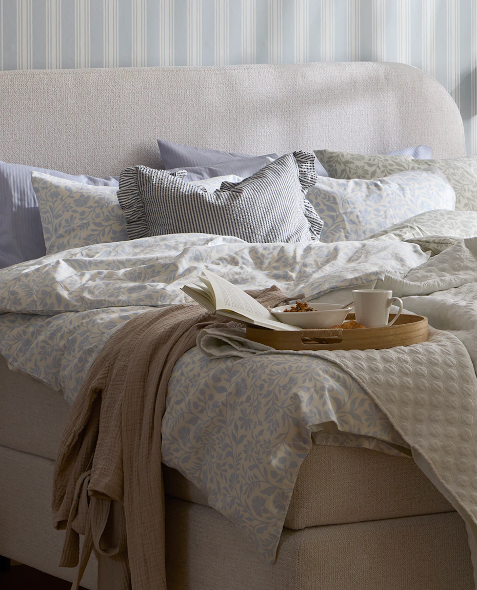 en grå kontinentalsäng med rundad gavel står i ett sovrum och är bäddad med påslakan i blåa toner