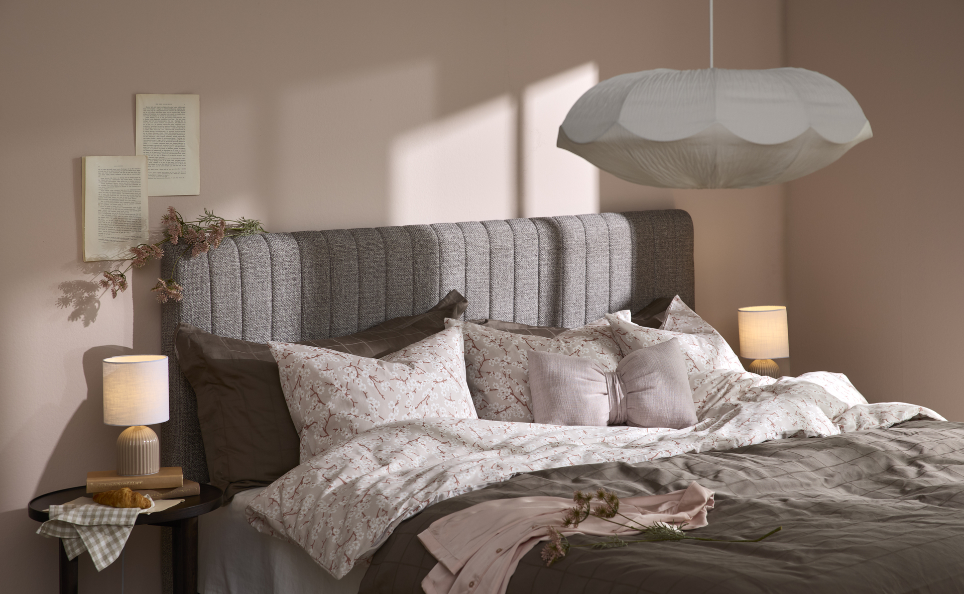 en grå kontinentalsäng med en gavel står i ett sovrum med rosa väggar. Sängen är bäddad med bruna och rosa-blommiga sängkläder. 