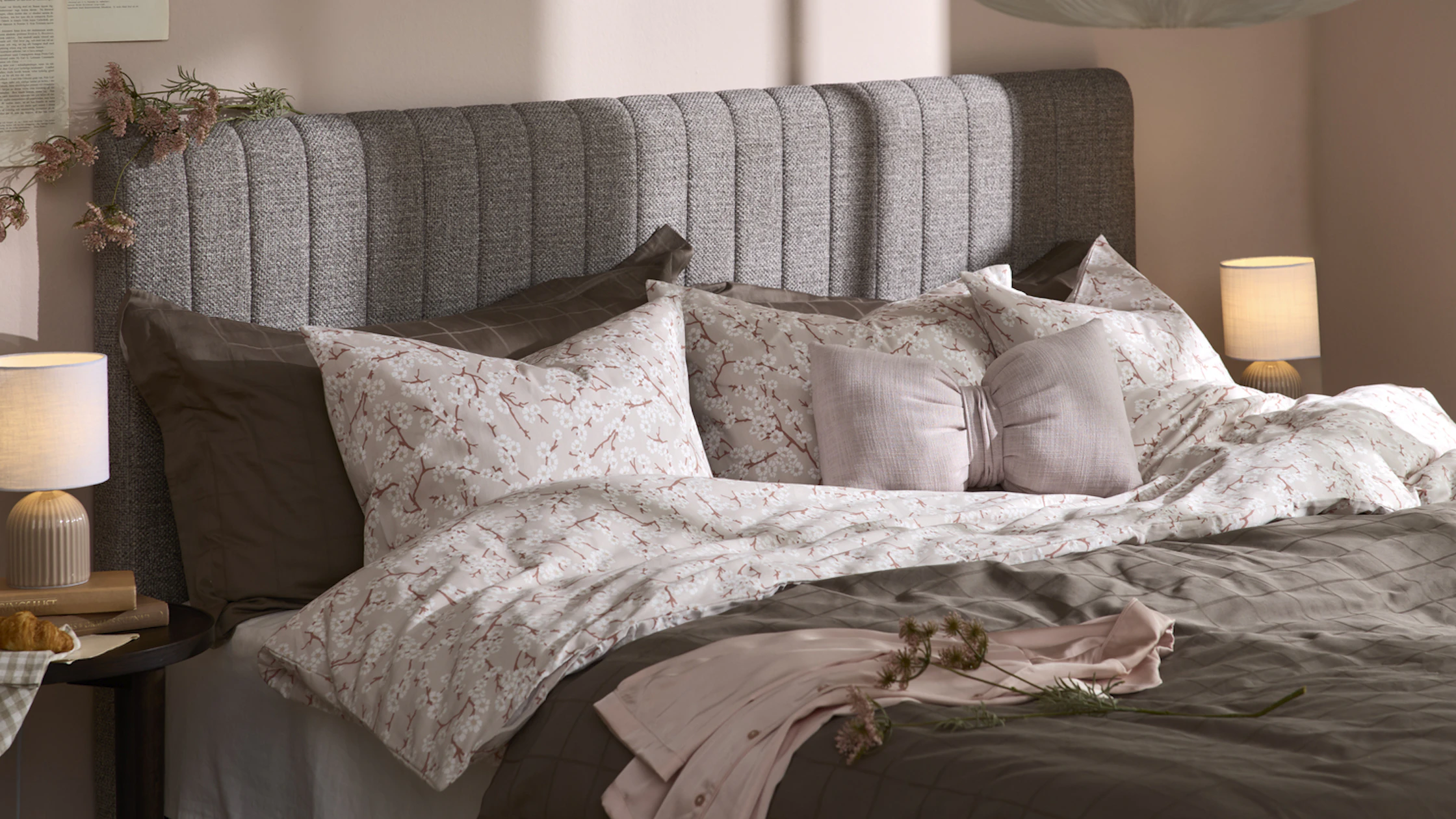 en grå kontinentalsäng med en gavel står i ett sovrum med rosa väggar. Sängen är bäddad med bruna och rosa-blommiga sängkläder.