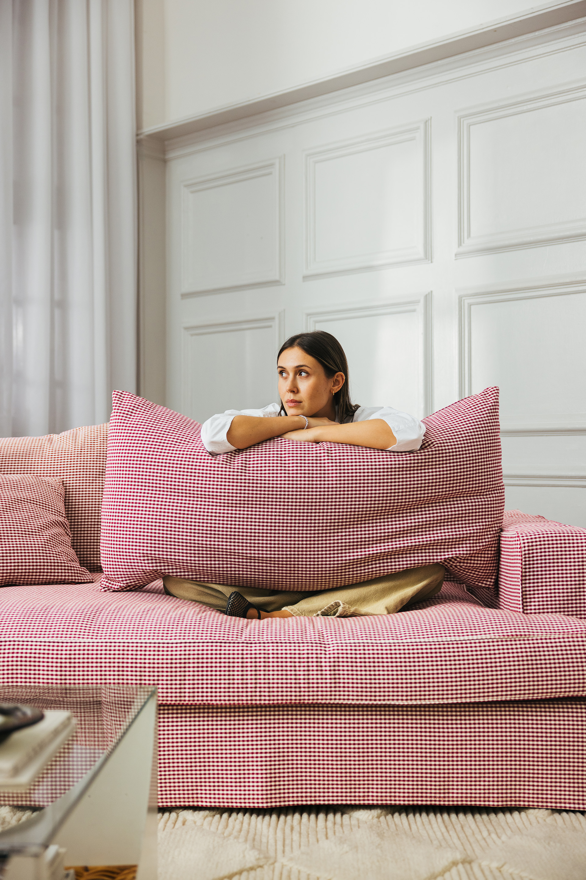 Kvinna tittar fram och hänger över ryggstödet på en soffa av rödvit randigt tyg. 