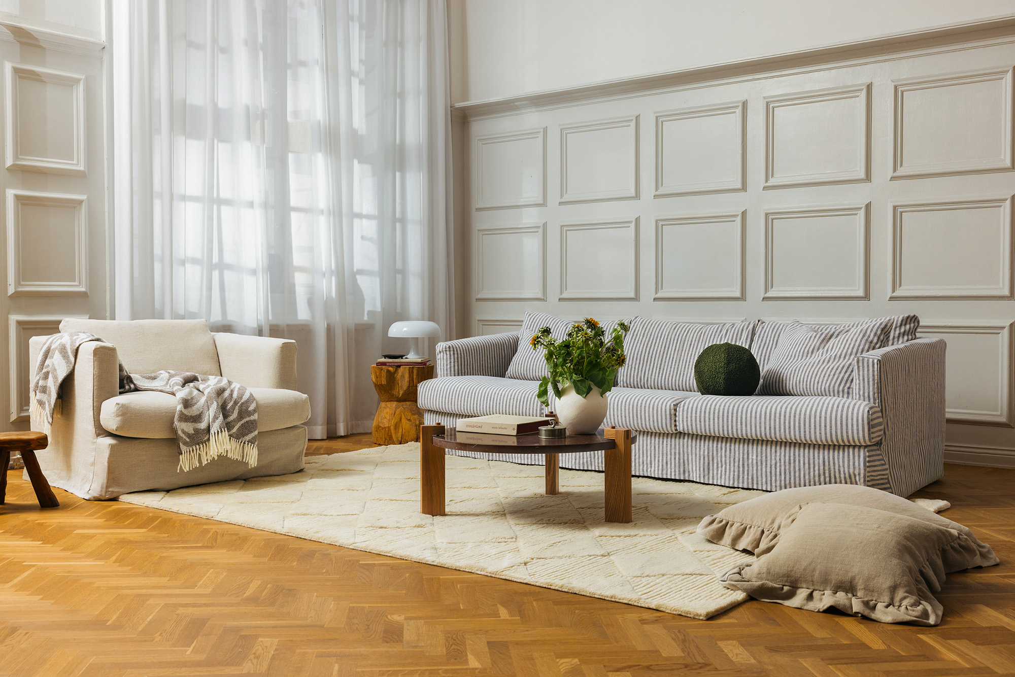 Vardagsrumsmiljö med stor soffa i blåvit randigt tyg och en cremefärgad fåtölj intill.