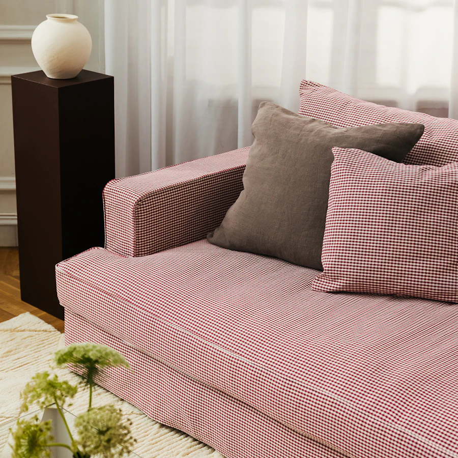 Del av soffa i vardagsrumsmiljlö där tyget är rödvit randigt och tre prdynadskuddar ligger ledigt i soffans hörn.