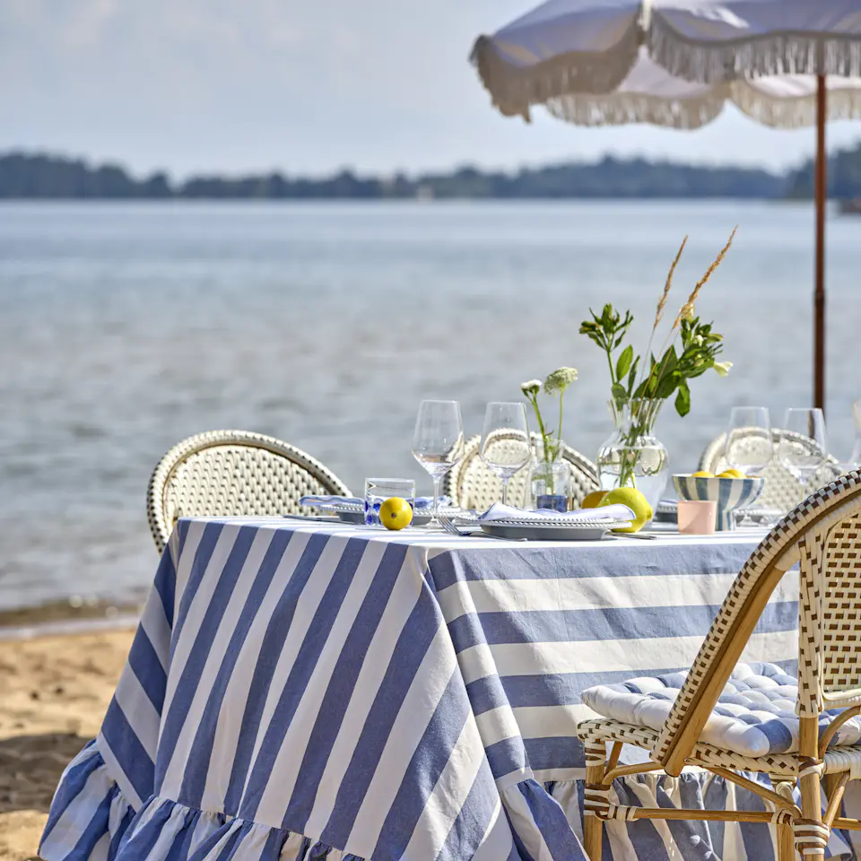 ett bord står dukat på en strand med en blårandig duk