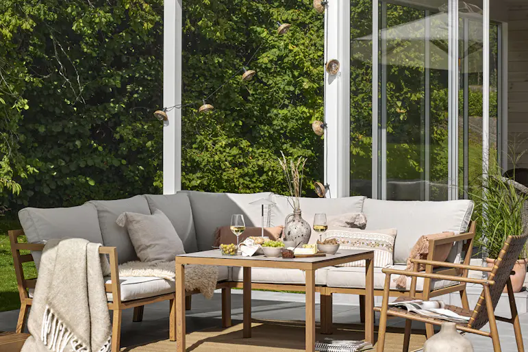 Uteplats med loungemöbler under ett vitt parasoll ståendes framför en pool med blått vatten.