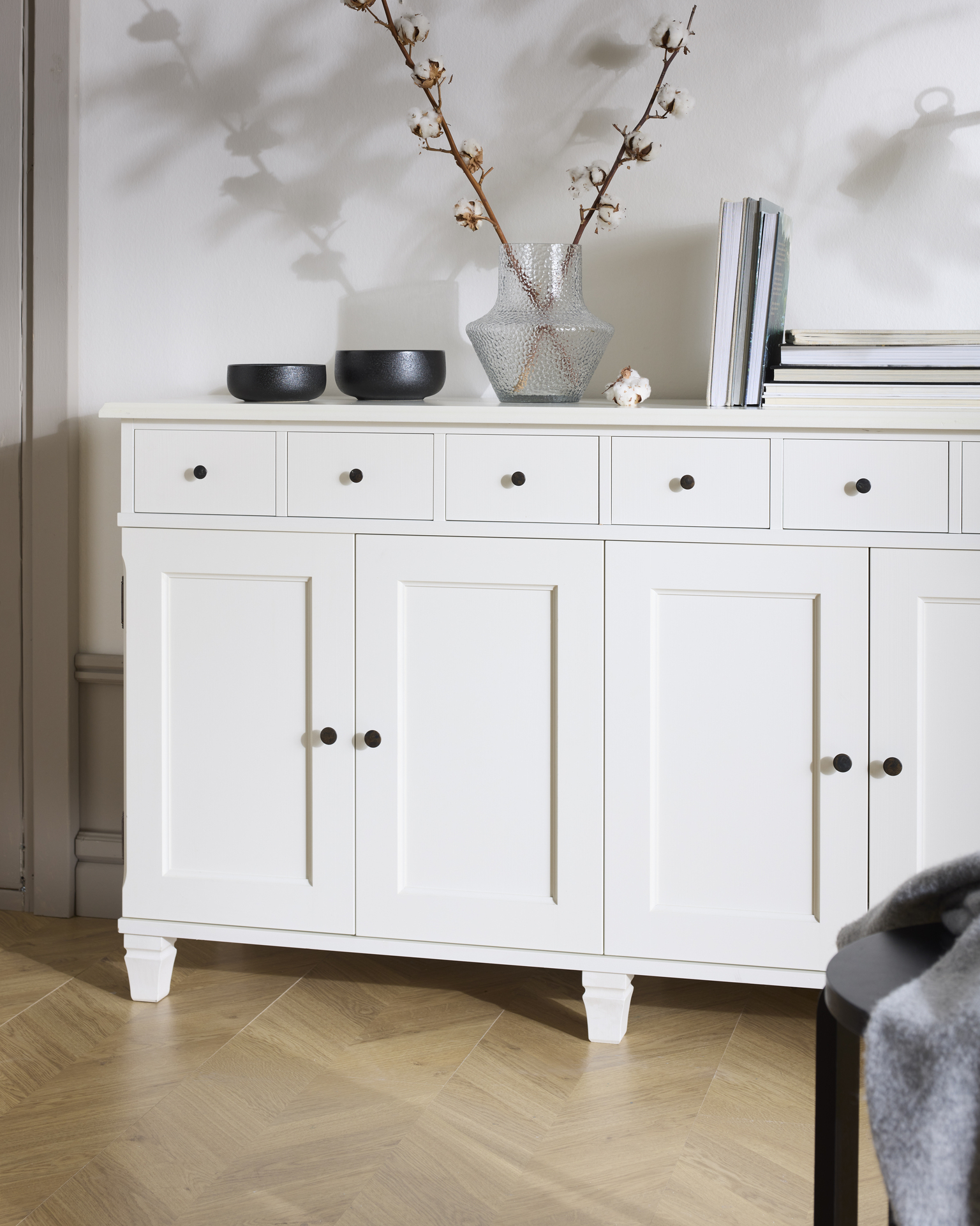 En vit skänk med två skåp och flera lådor står framför en vit vägg.