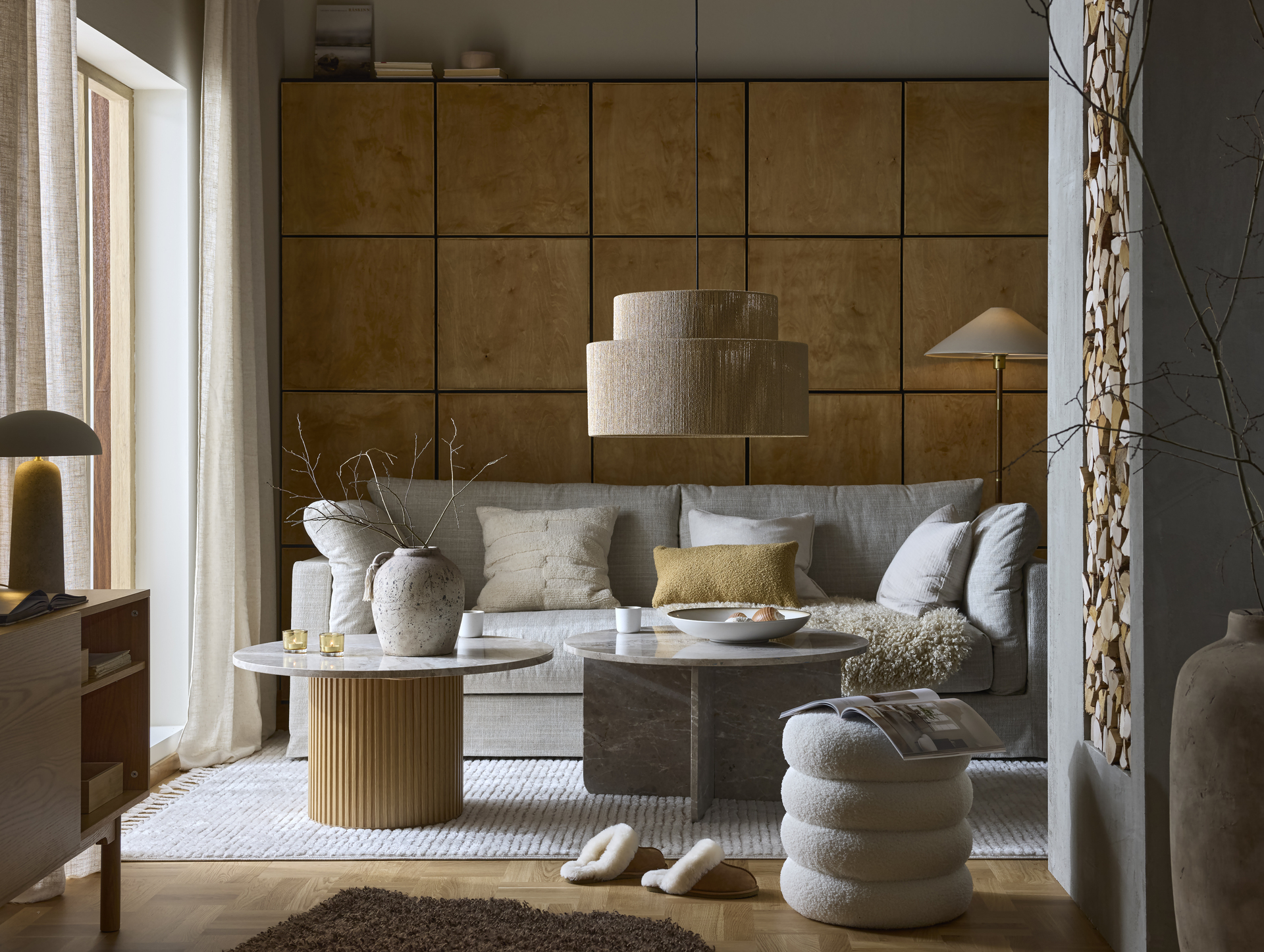 ett vardagsrum där det står en beige soffa samt två runda soffbord i marmor