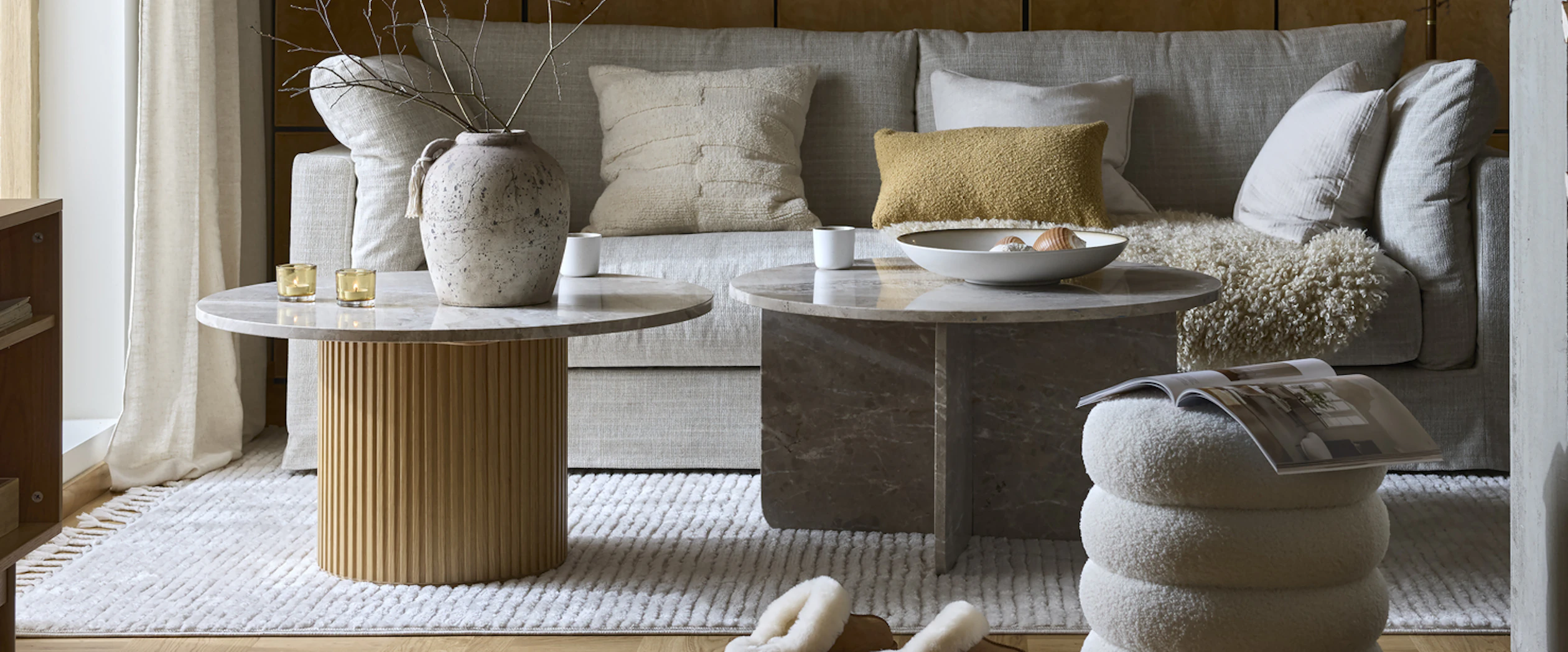 ett vardagsrum där det står en beige soffa samt två runda soffbord i marmor