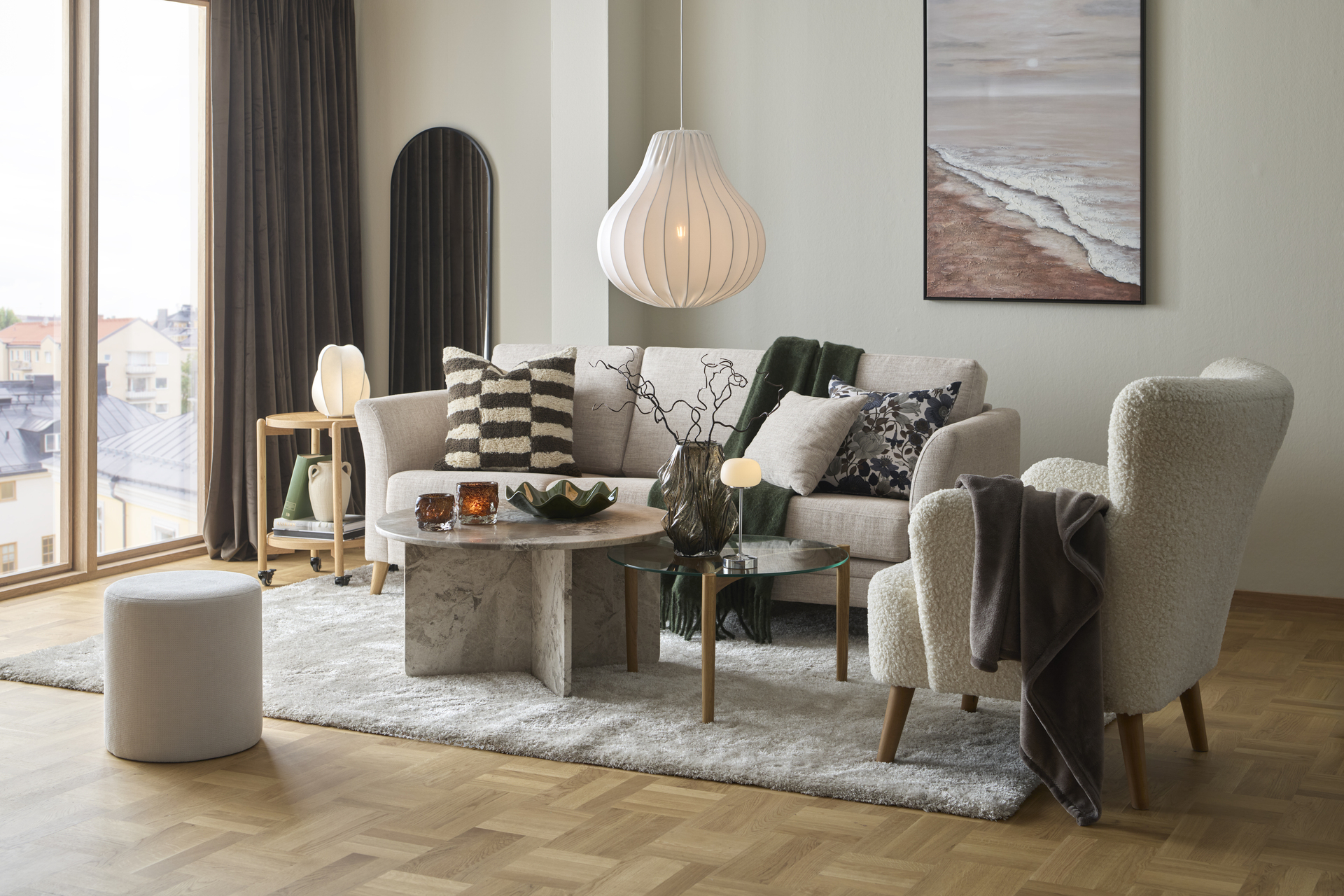 Ett vardagsrum där det står en beige soffa, fåtölj, soffbord i marmor och en stor vit matta