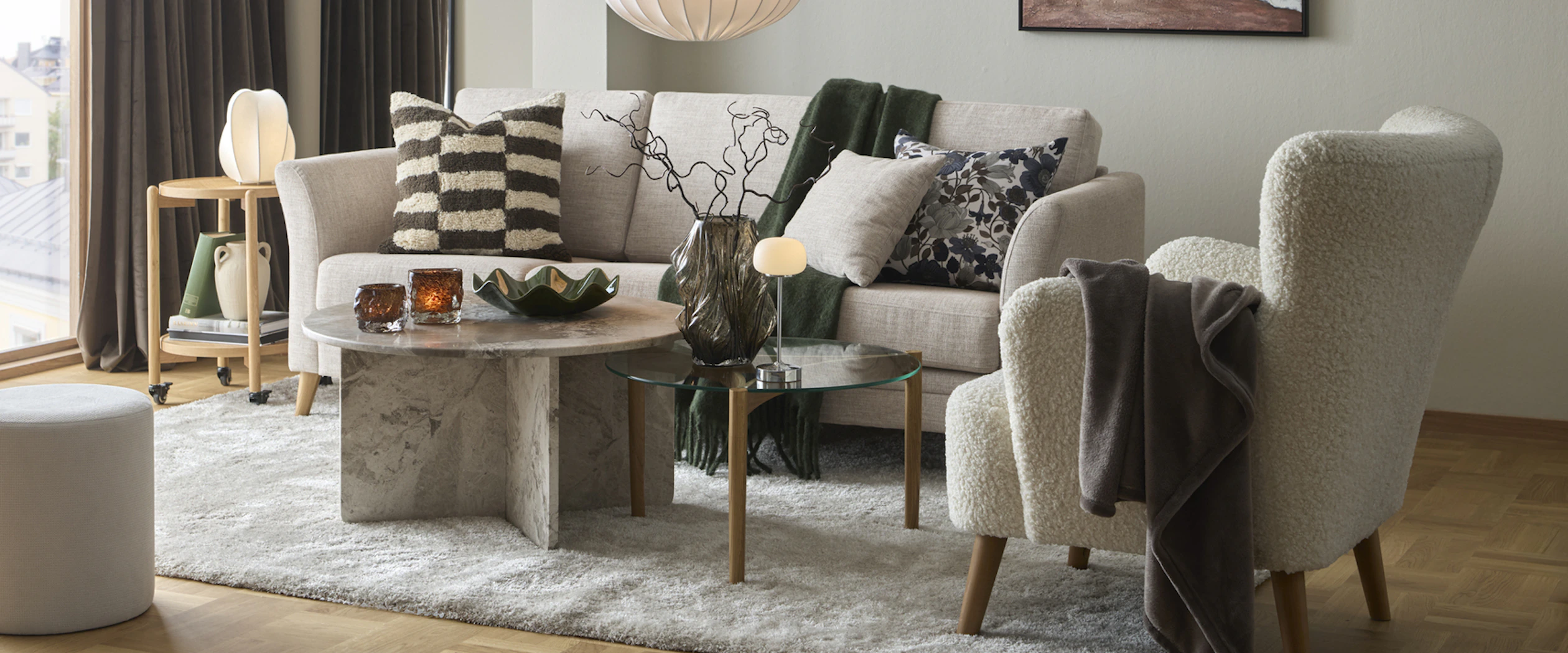 Ett vardagsrum där det står en beige soffa, fåtölj, soffbord i marmor och en stor vit matta