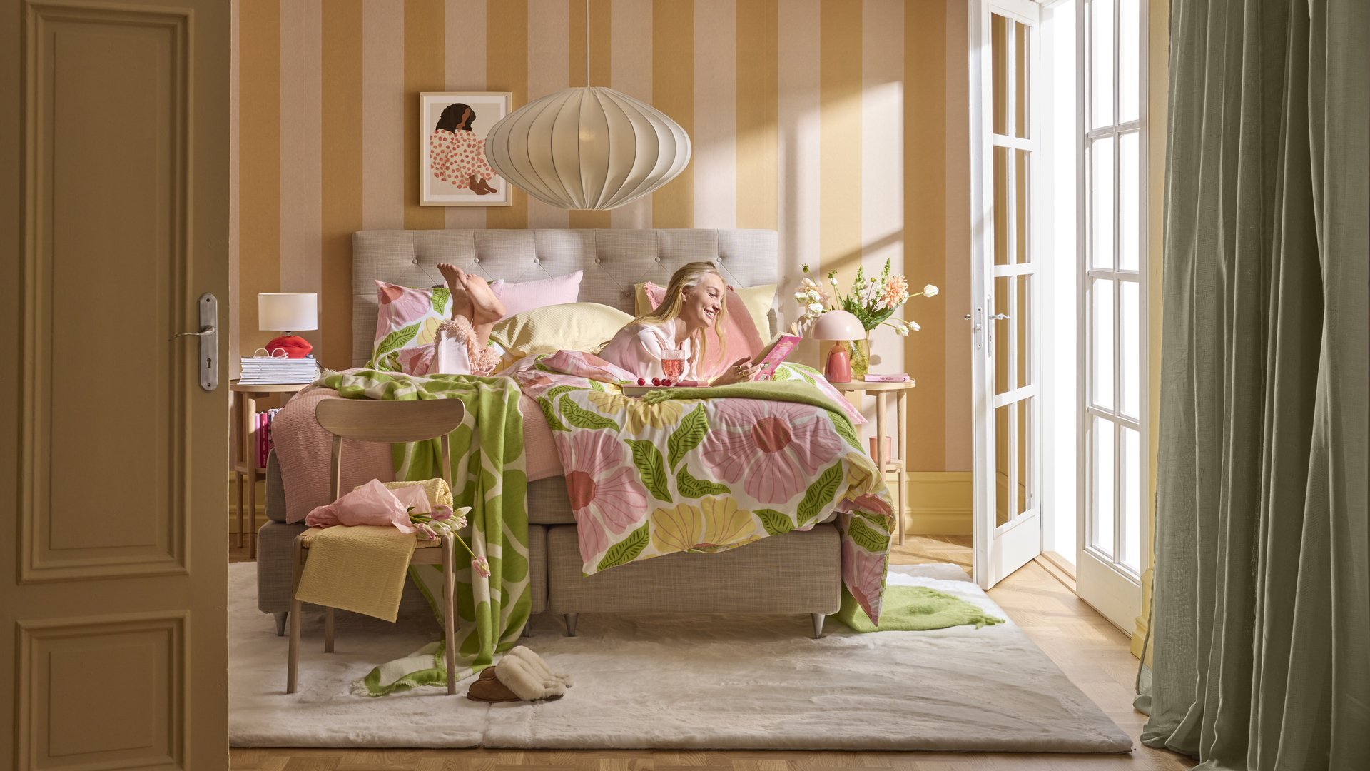 en blond tjej ligger i en beige säng i ett färgglatt sovrum och läser en bok