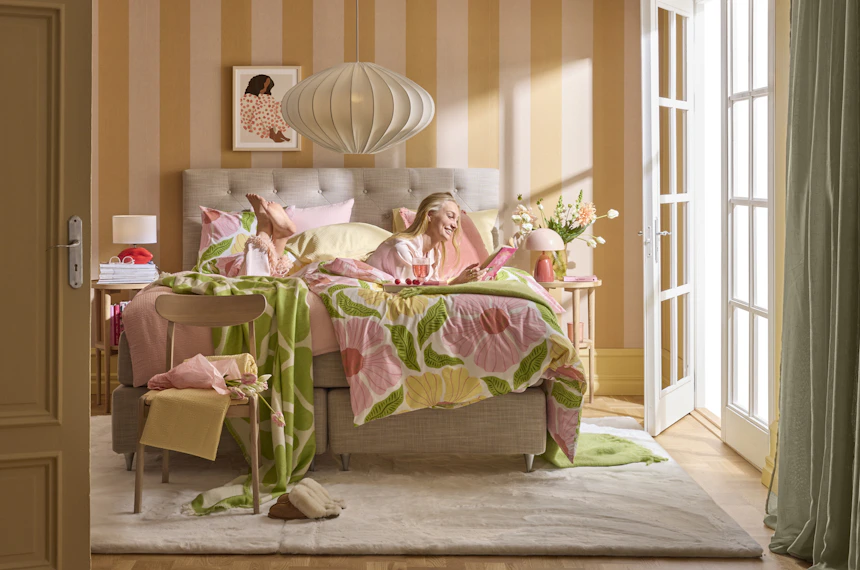 en blond tjej ligger i en beige säng i ett färgglatt sovrum och läser en bok