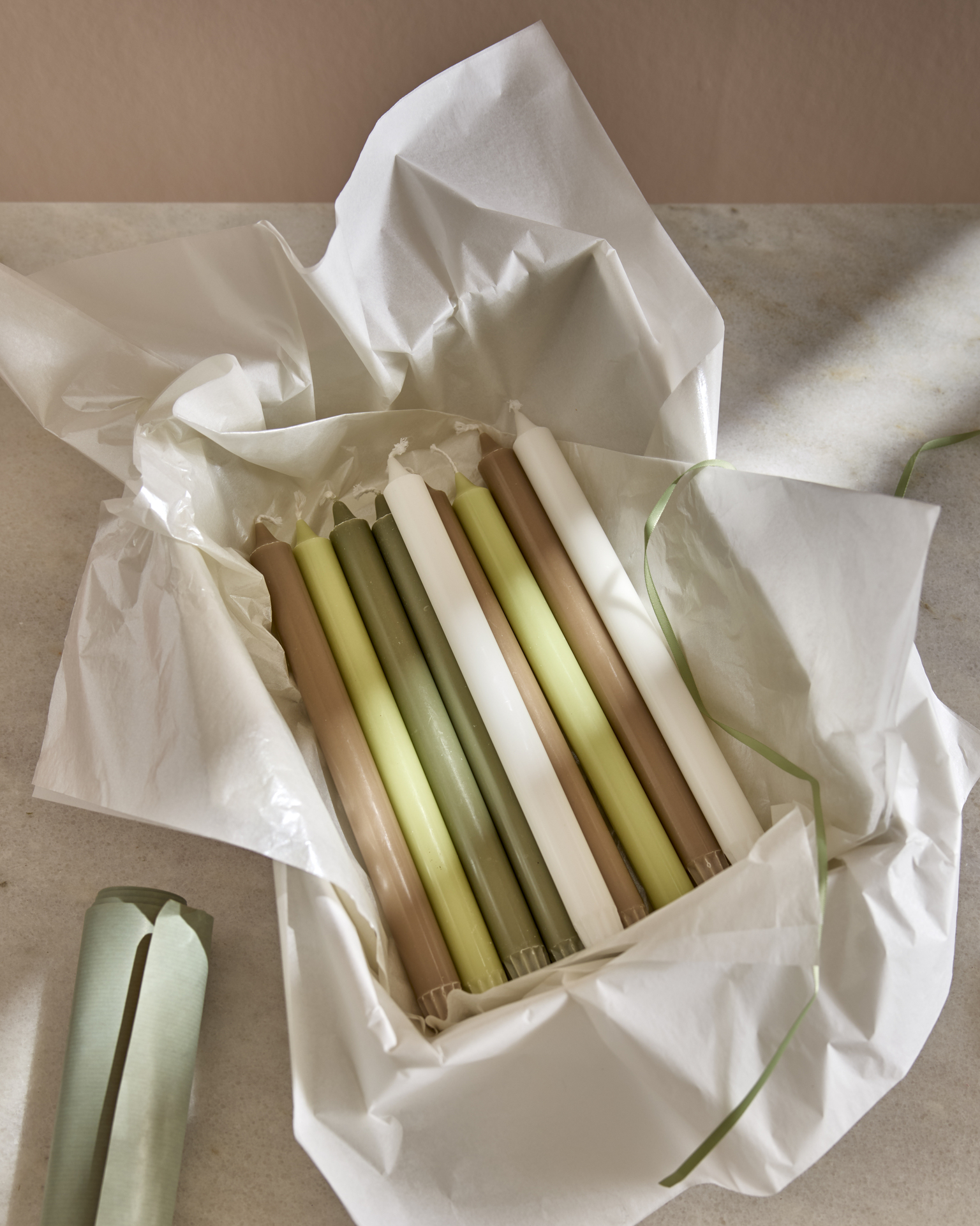 Flera rustikljus i vitt, grönt och brunt ligger i papper.