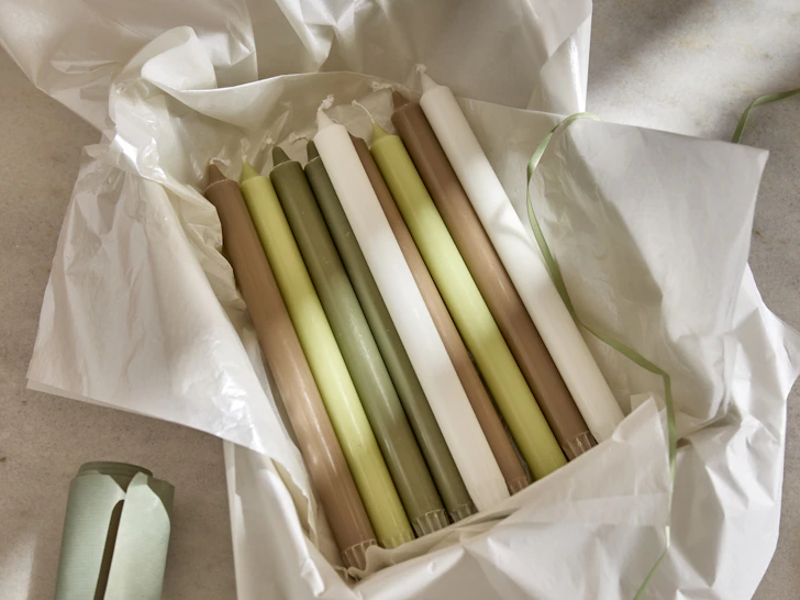 Flera rustikljus i vitt, grönt och brunt ligger i papper.