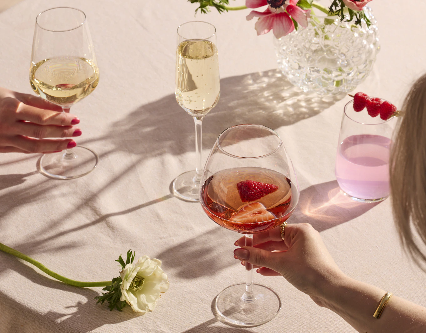Flera festliga glas med olika innehåll är placerade på en rosa duk.