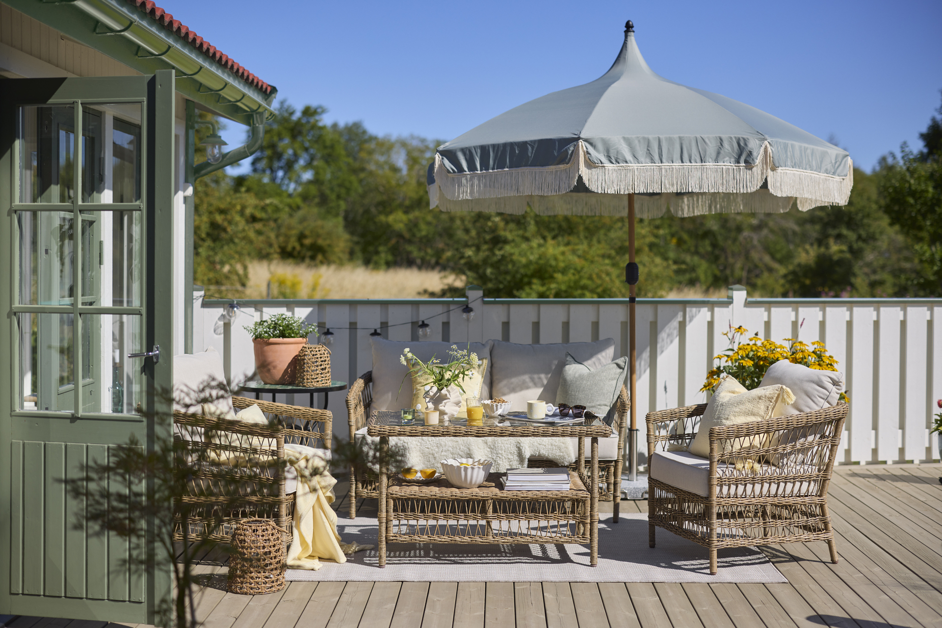 En loungegrupp i konstrotting står i solen på en altan, på soffbordet står en frukost uppdukad