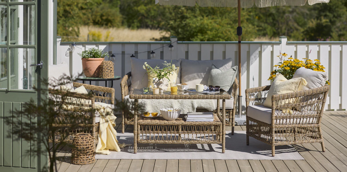 En loungegrupp i konstrotting står i solen på en altan, på soffbordet står en frukost uppdukad