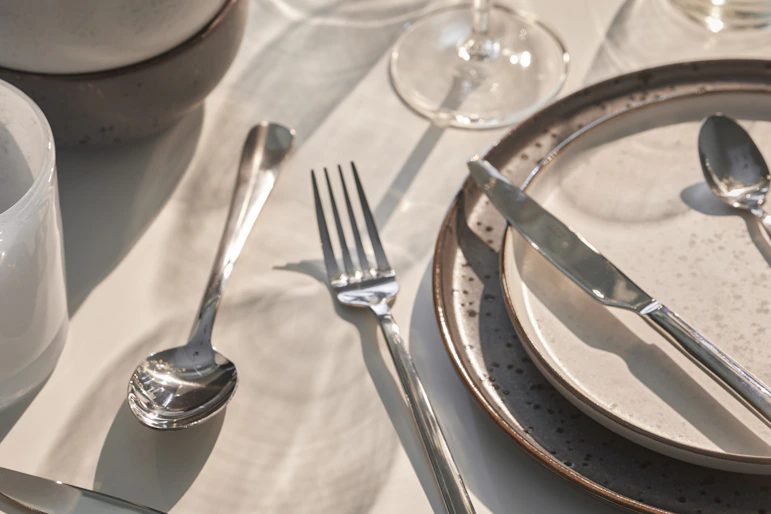 Flera bestick ligger utspridda på ett bord dukat med ljust porslin och en vit duk.