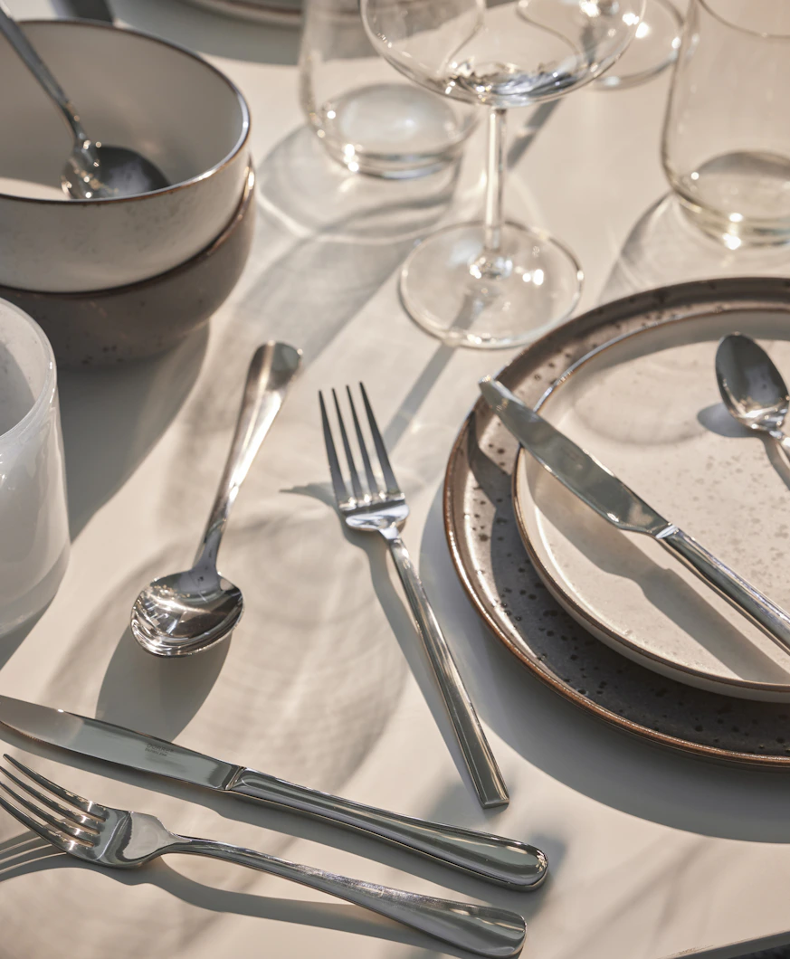 Flera bestick ligger utspridda på ett bord dukat med ljust porslin och en vit duk.