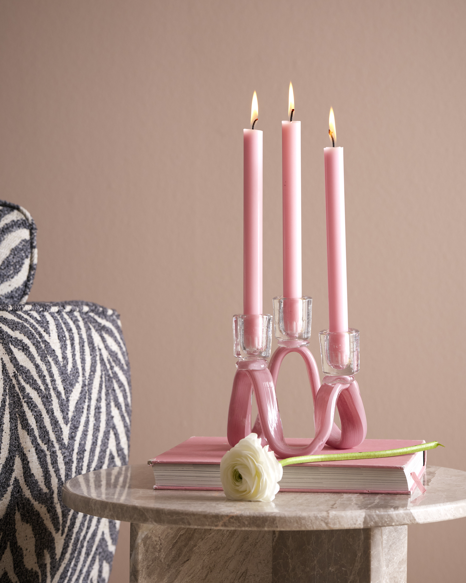 En rosa ljusstake med tre rosa ljus står bredvid en zebrarandig soffa.