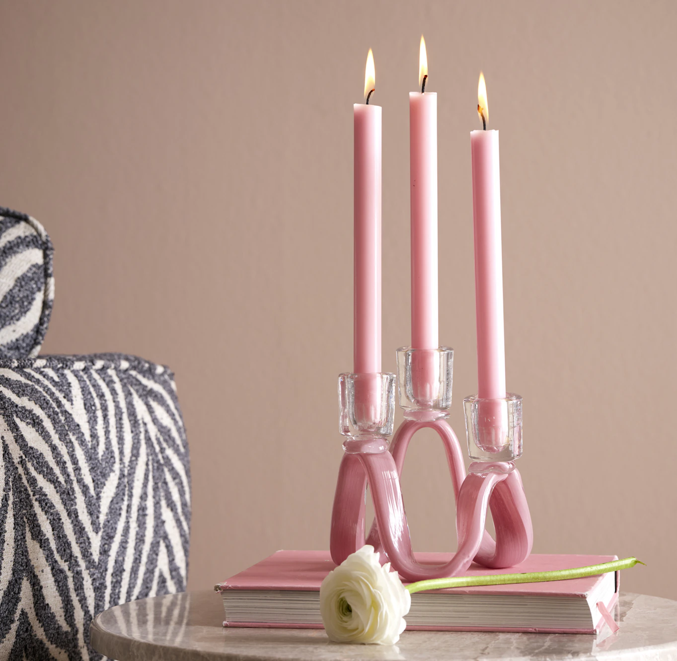 En rosa ljusstake med tre rosa ljus står bredvid en zebrarandig soffa.