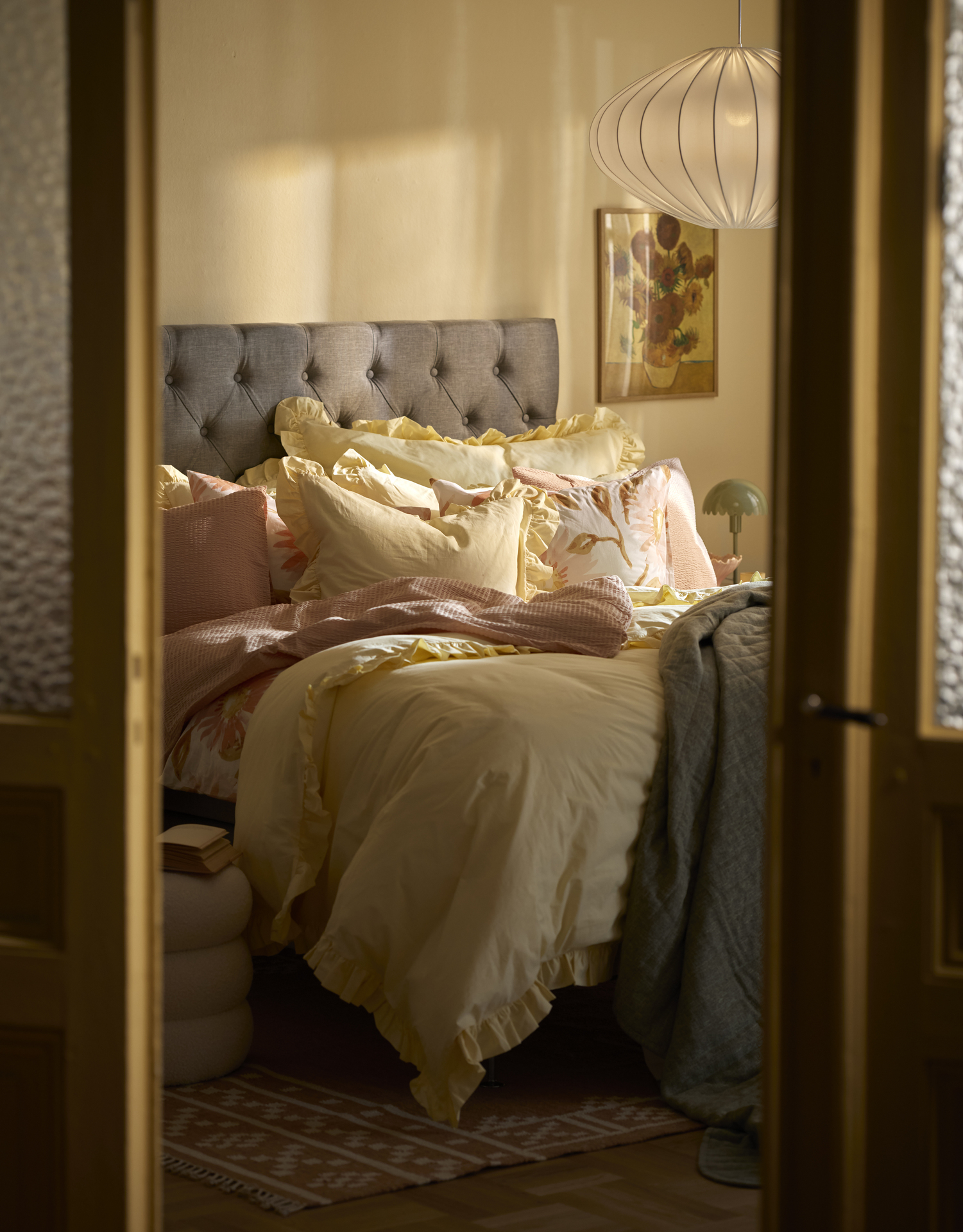En grå kontinentalsäng står i ett sovrum och är bäddad med påslakan i rosa och gult
