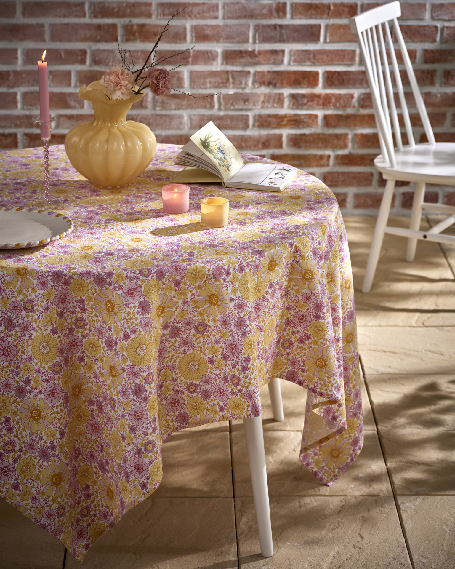 i ett uterum står ett bord med en blommig duk i rosa och gult