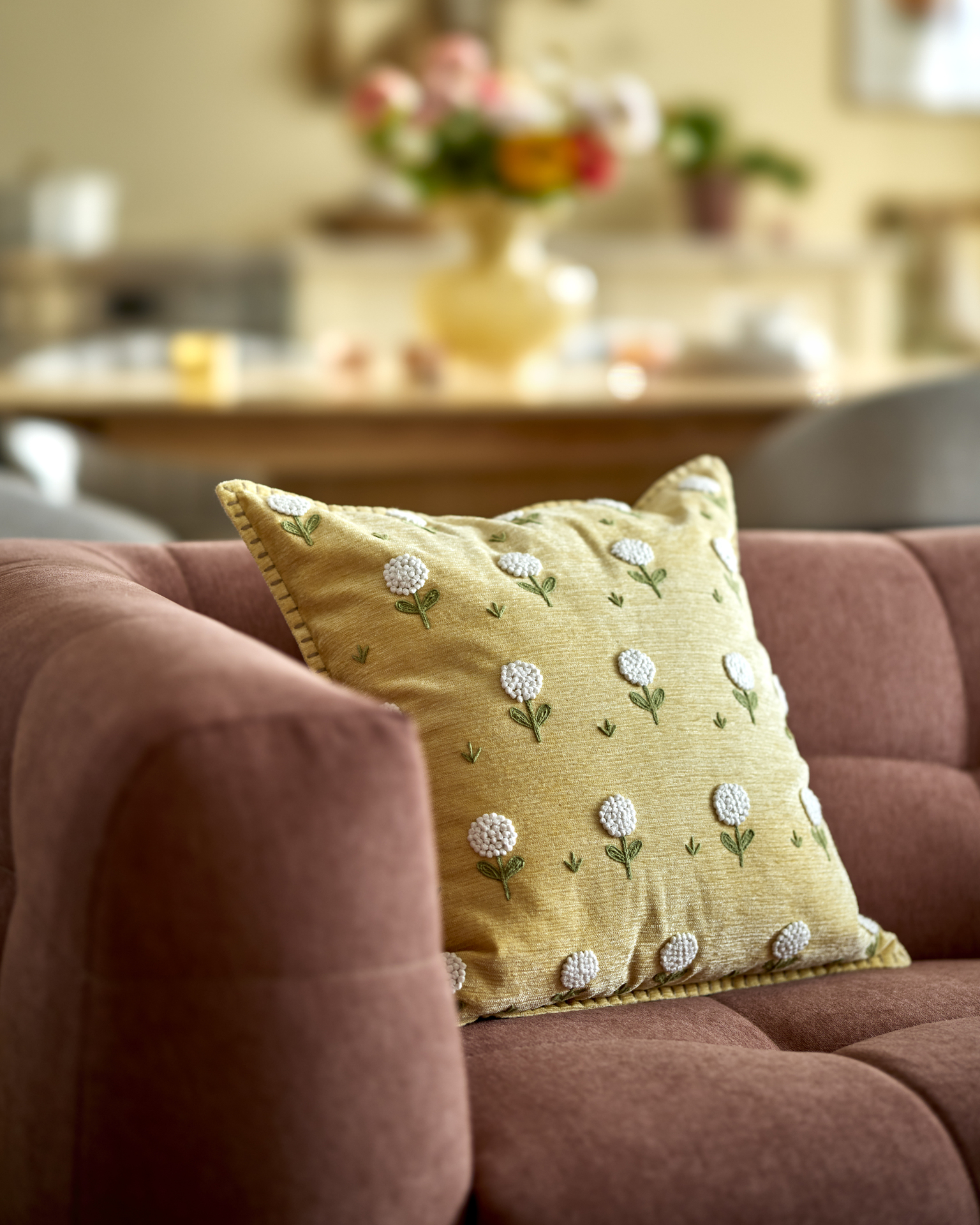 I en rosa soffa ligger en gul kudde med vita blommor på