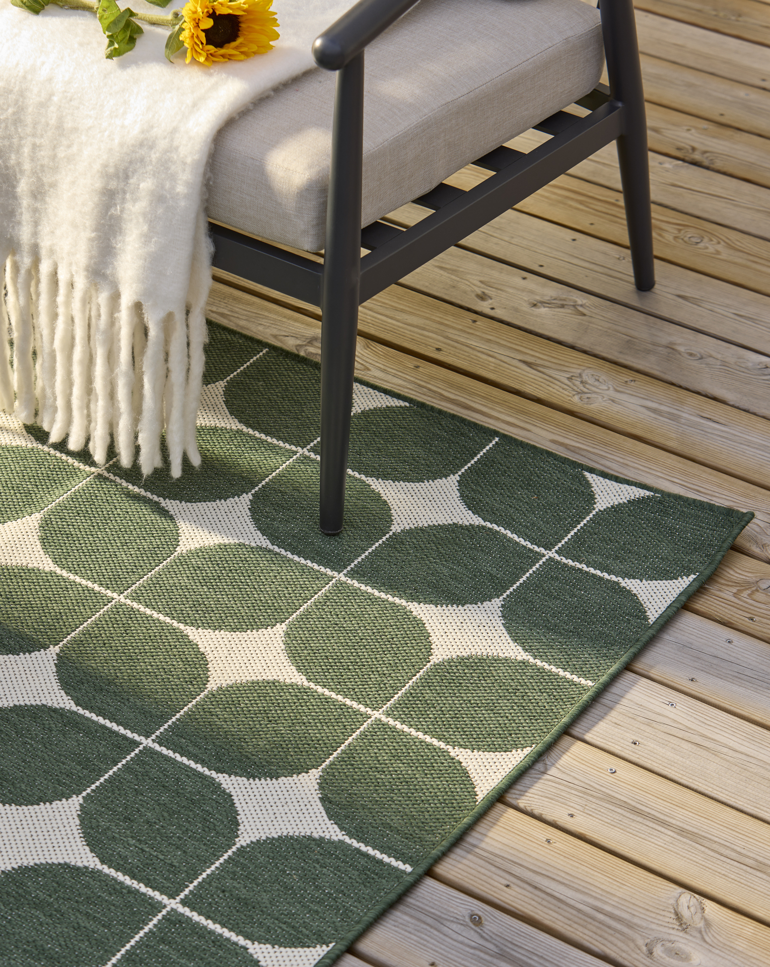 En grönmönstrad utematta ligger på en altan under en utefåtölj