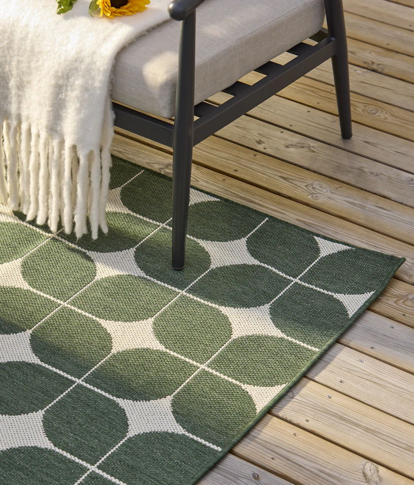 En grönmönstrad utematta ligger på en altan under en utefåtölj