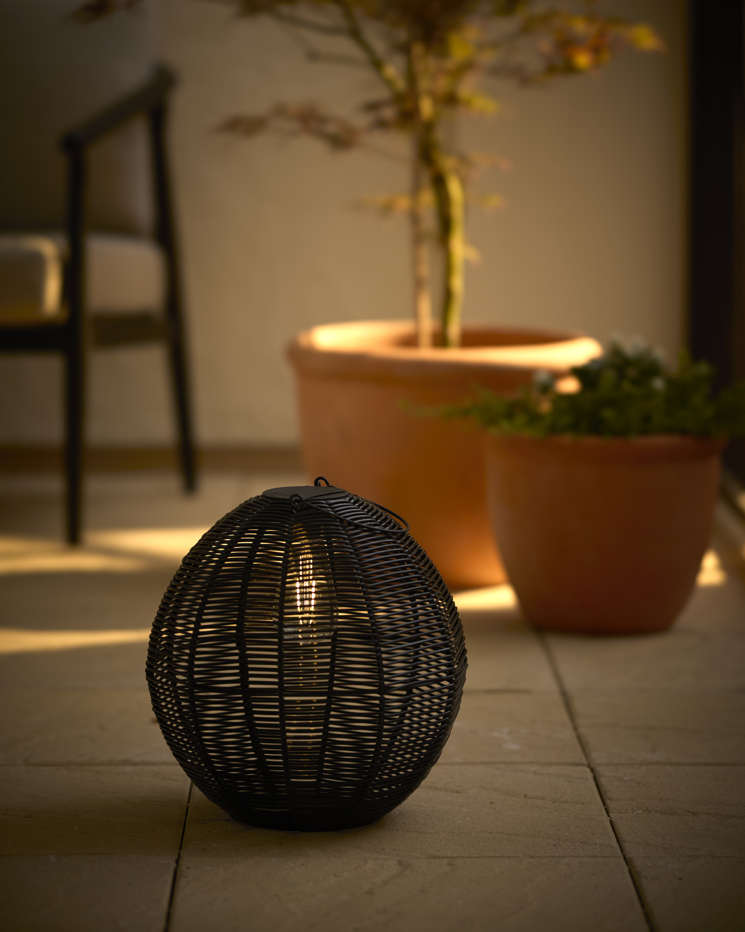 en svart solcellslampa står på en uteplats framför två utekrukor