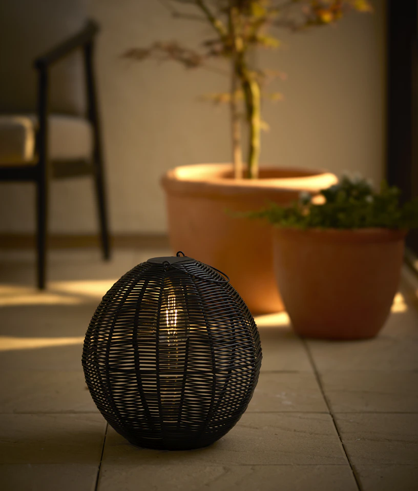 en svart solcellslampa står på en uteplats framför två utekrukor