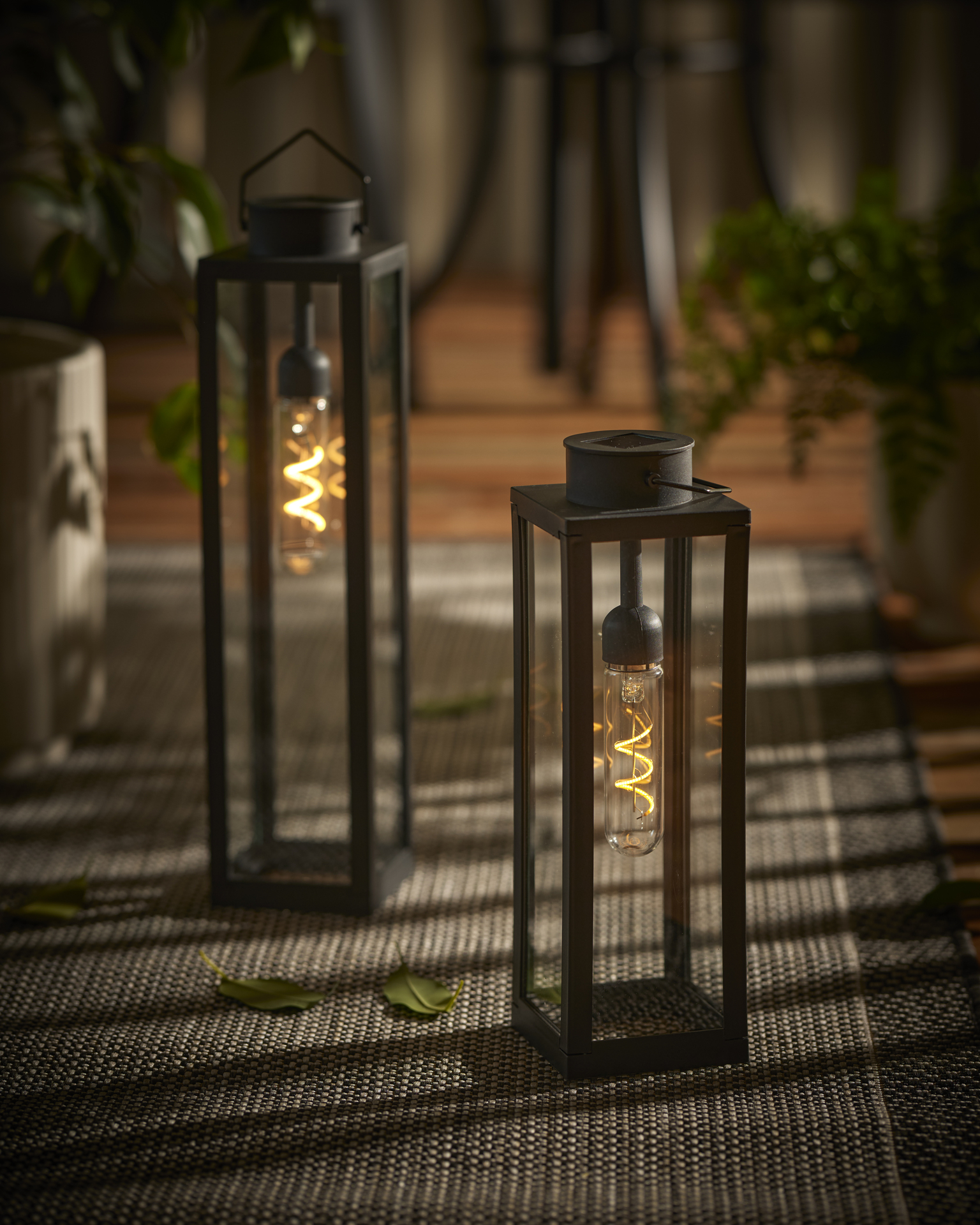 Två svarta ljuslyktor står på en uteplats i skymningen