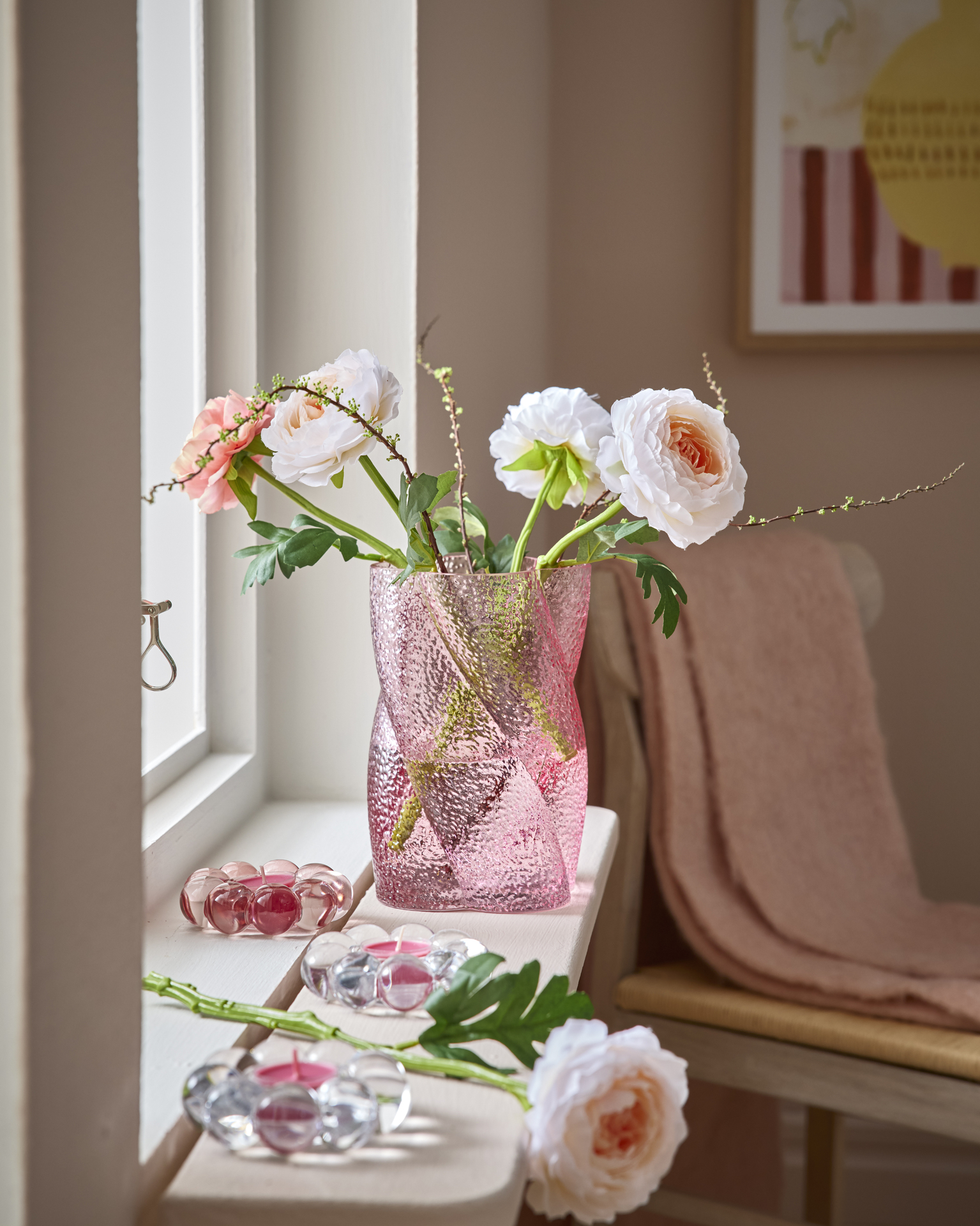 En rosa vas med konstblommor står på en fönsterbräda