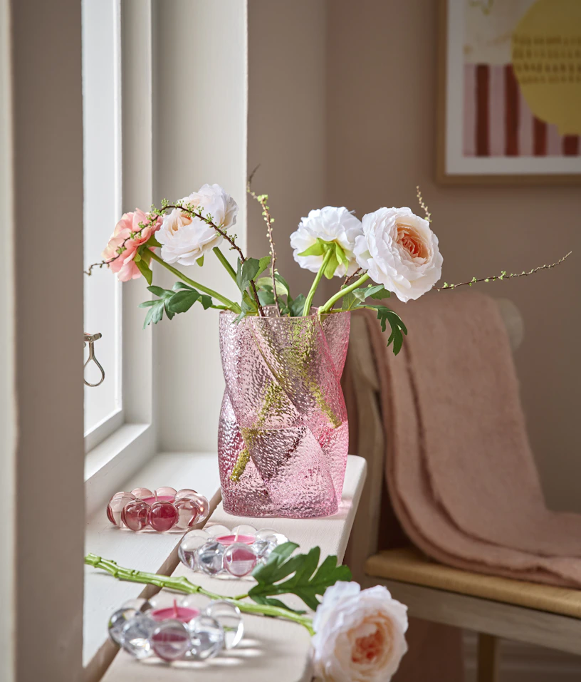 En rosa vas med konstblommor står på en fönsterbräda